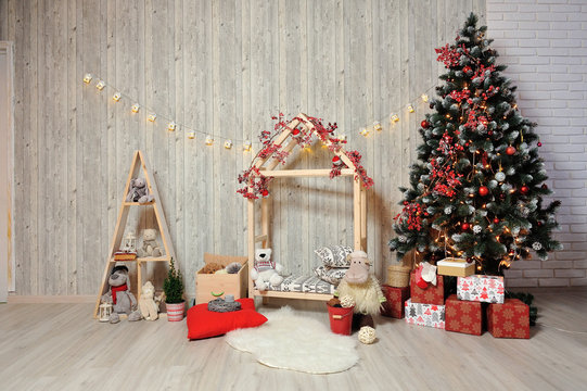 New Year or Christmas photo zone for children. Children's photo zone with a wooden house, toys, a Christmas tree and gifts in a warm light