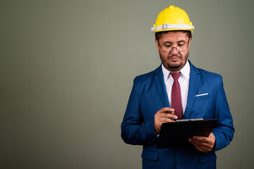 Bearded Persian businessman wearing hardhat against colored back