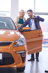 Naklejka premium Dealer stands near a new car in the showroom