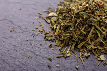dried tarragon and essential oil on a dark stone background