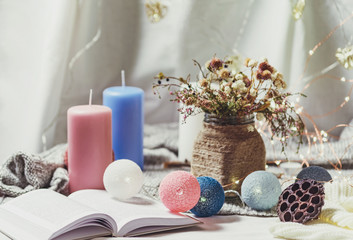 Romantic winter and New Year's style interior view with a candle, book, garland and dryed flowers in rustic vase