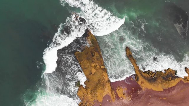 Descending spinning aerial shot of waves crushing in to a huge cliff at the ocean coastline