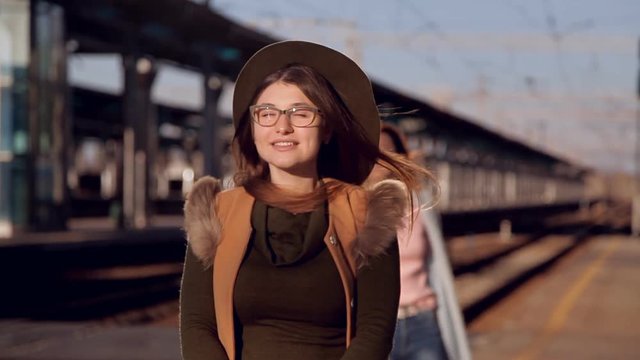 The wind blows off the girl's hat. Girl in a hat and glasses at the railway station waiting for the train