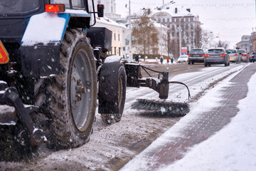 Tractor with rotating brush cleaning road from fallen snow. Industrial street sweeper machine with...