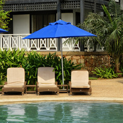 Beach umbrella and sun beds close to a swimming pool on tropical house background. Luxury resort. Summer relax. Travel and vacation at exotic place.