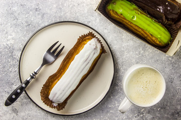 eclairs on white plate with cup of latte coffee on grey table. Top view.
