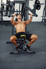 Fototapeta na wymiar A strong young man pumping up his chest muscles in an exercise machine. Sporty and healthy concept.