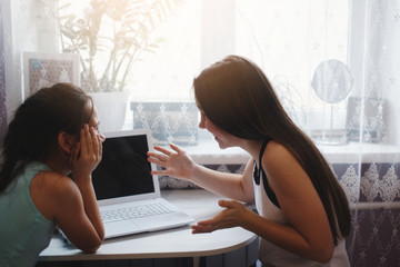 Two girls sit at the table and work with a laptop.