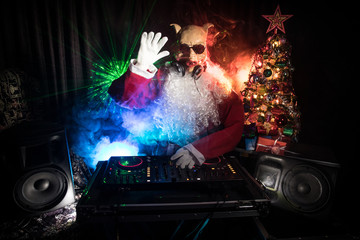 Fototapeta na wymiar Dj Santa Claus at Christmas with glasses and snow mix on New Year's Eve event in the rays of light.
