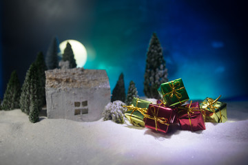 Christmas and New Year miniature house in the snow at night with fir tree. Little toy house on snow with tree. Festive background. Christmas decorations.