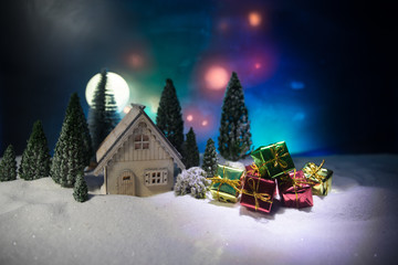 Christmas and New Year miniature house in the snow at night with fir tree. Little toy house on snow with tree. Festive background. Christmas decorations.