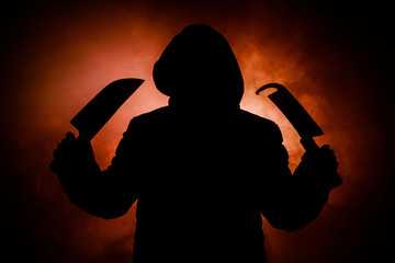 A dangerous hooded man standing in the dark and holding a knife. Face can not be seen. Committing a crime concept. Selective focus