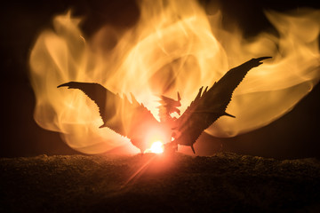 Silhouette of fire breathing dragon with big wings on a dark orange background