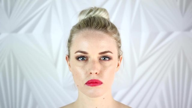 Slow motion of milk poured over a young beautiful girls' face standing in front of an abstract background