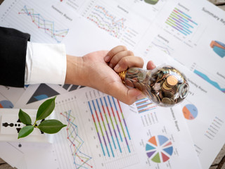 Top View Hand of businessman hold light bulb with coin and calculator on business graph. Concept of...