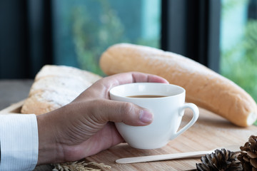 Hands of businessman holding cup of coffee and breakfast bread. Health breakfast