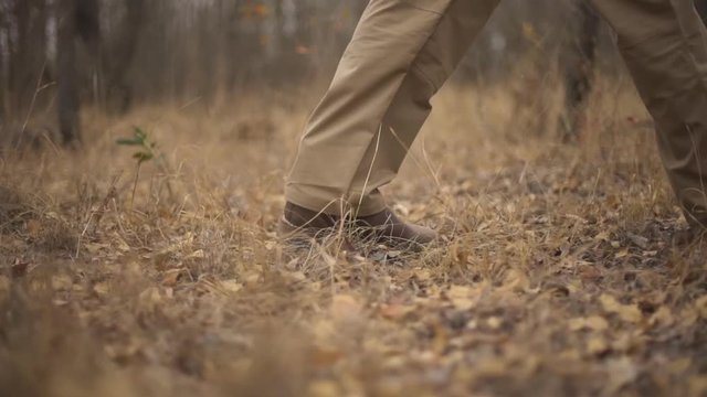 Low angle shot with only the boots visible of three men in camouflage walking through the bush tracking a deer to hunt
