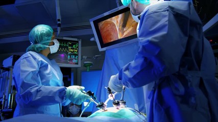 European Medical surgeons training by performing laparoscopic surgery on the patient in operating theatre using video camera technology  - Powered by Adobe