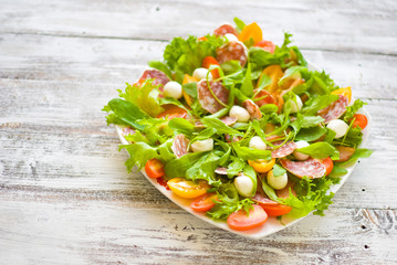 Arugula salad \ Salad with rocket salad, cherry, olives, cheese, mozzarella, blue cheese, sausage on a light wooden background