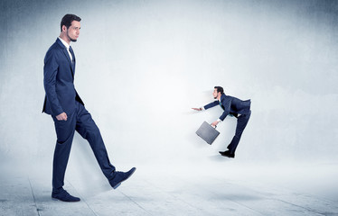 Big businessman kicking small businessman who is flying away with his briefcase on his hand

