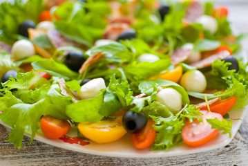 Arugula salad \ Salad with rocket salad, cherry, olives, cheese, mozzarella, blue cheese, sausage on a light wooden background