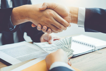 Corruption concept,Business man passing money dollar bills corruption bribery to businessman manager and handshake between two colleagues.