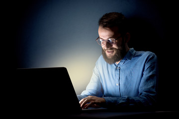 Young handsome businessman working late at night in the office with a dark background