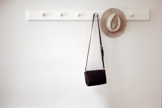 Stylish hat and small black purse hanging on white pegs on wall in cozy room