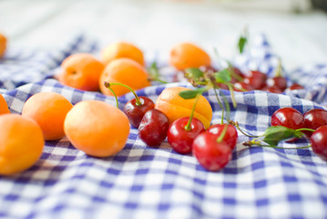 Fresh Fruits: cherry and apricots on a light blue checkered napkin background