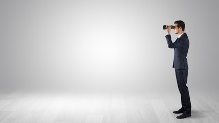 Businessman looking forward with binoculars in an empty space
