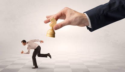Small frail businessman with suitcase running away from big hand with chessman concept
