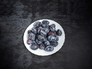 Plate with ripe prunes on a dark background