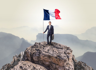 Successful businessman on the top of a mountain holding France victory flag
