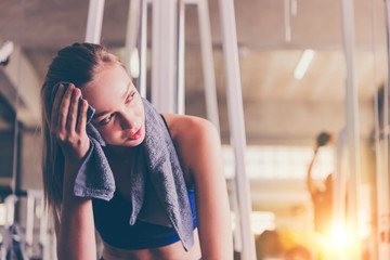 Tired woman from workout wiping sweat with towel in sports gym 