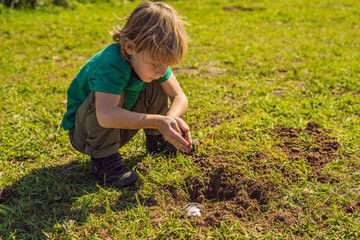 The boy plays recycling. He buries plastic disposable dishes and biodegradable dishes