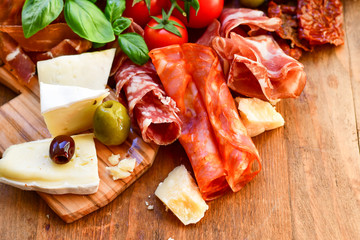  italian appetizer with prosciutto, parmesan cheese and brie cheese, sun-dried tomatoes, salami, green olives and basil, wooden table, Italian restaurant, selective focus