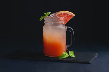 Ice cold citrus cocktail in a vintage glass mason jar. Dark background with copy space for a menu.