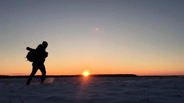Backpacker walking on snow mountain in winter. Hiker walks in snow at sunset. Man with backpack trekking in mountains. Winter hiking.