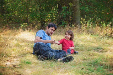 Naklejka na ściany i meble A child girl with her dad lying on the grass are looking at the grass and spikelets. Concept - family relations, child upbringing and development