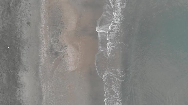 Aerial Flat-lay view of chaos of undertow waves motion in the dark sandy beach shore	