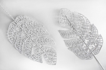 Silvery glittering monstera leaves on silver background. Festive decoration. Tropical Christmas...
