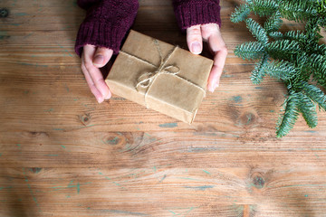 Top view of woman hands with simple gift box and christmas fir tree on wooden background
