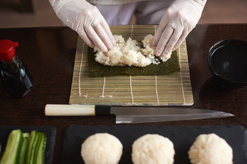 Close-up view of process of preparing rolling sushi. Nori and white rice. Chef's woman hands touch rice. Chef starts cooking sushi