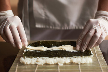 Close-up view of process of preparing rolling sushi. Nori, white rice and chees on bamboo mat. Chef starts cooking sushi rolls