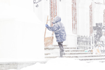 Woman cleaning snow with shovel in winter day. Snow storm
