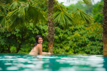 young attractive and beautiful Asian Chinese woman relaxing happy at tropical beach resort swimming at jungle infinity pool enjoying Summer holidays in paradise island