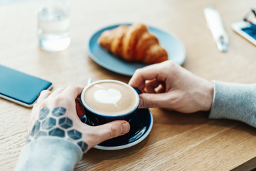 Man hands holding cup of coffee. Croissant and mobile phone are on background.