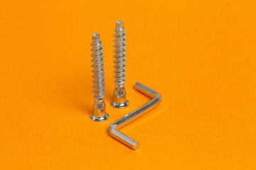 Metal hex key and hexagonal screws. Close-up on orange background