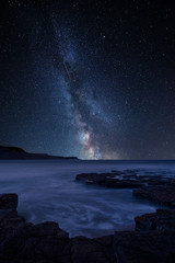 Vibrant Milky Way composite image over landscape of coastline and rocky shore