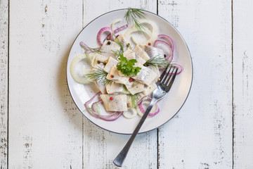 Herring pickle with onion, oil, pepper and dill on plate.